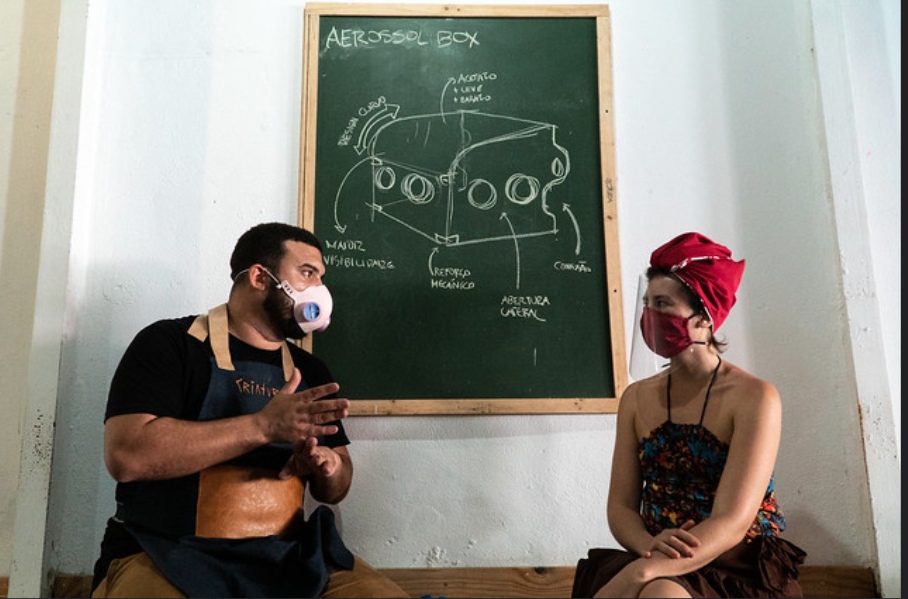 Picture showing two people sitting on a bench in front of a chalk board that shows a drawing of the "Aerosol Box"